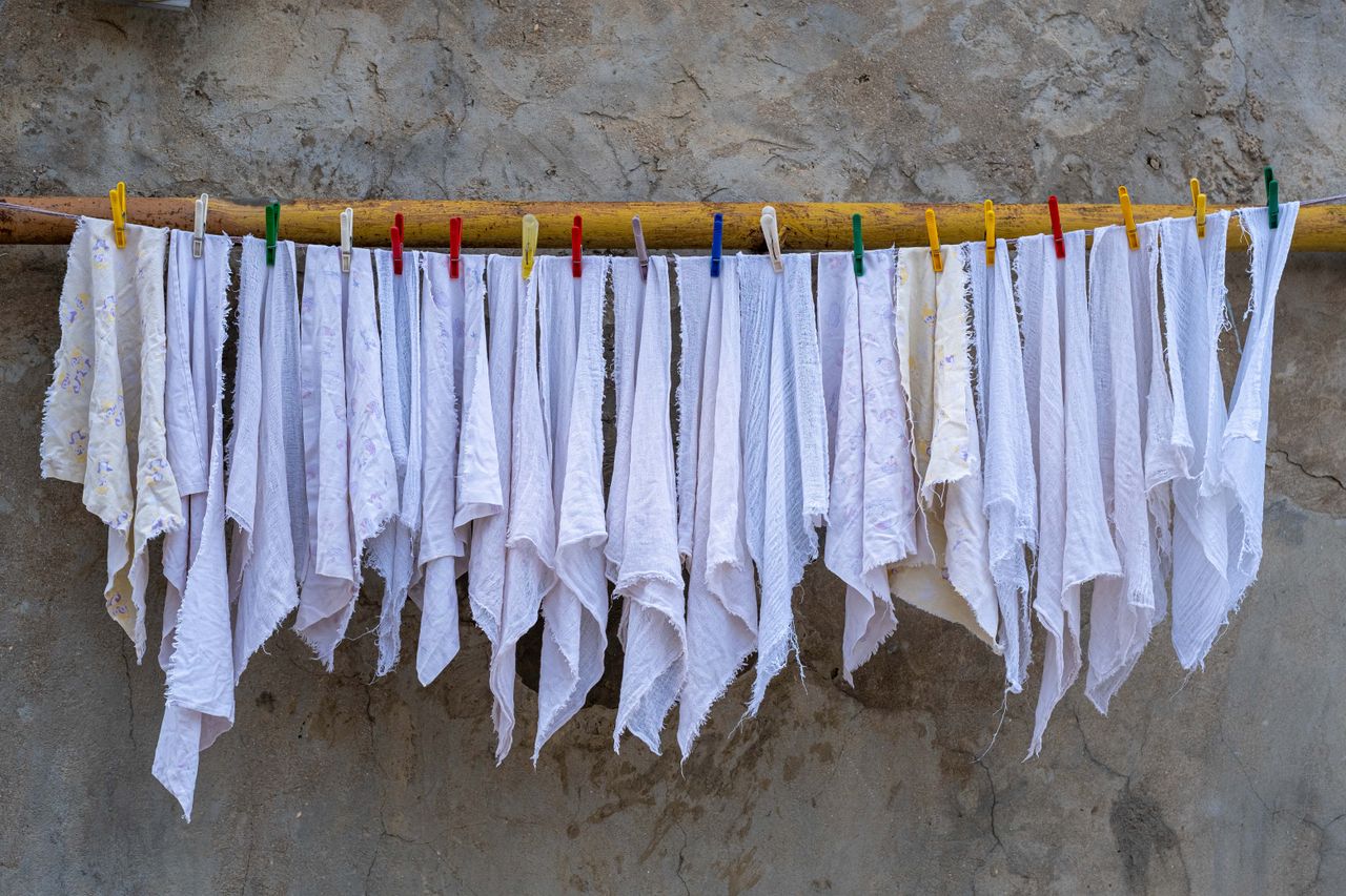 Blanchisserie à Nice : le guide pour un linge frais et bien entretenu Neatly arranged white fabrics drying under the sun, held by colorful clothespins against a rustic wall.