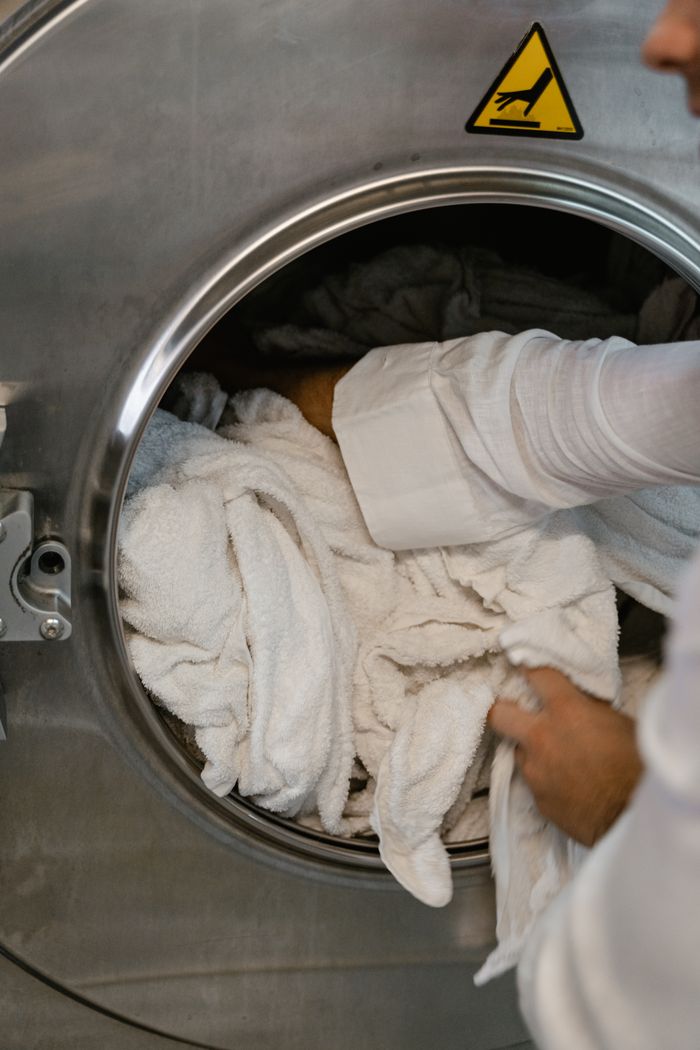 Close-up of hands loading white towels into a large industrial washing machine at a laundromat.